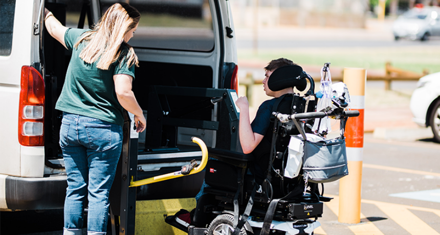 A young man in a wheelchair getting assistance into the car